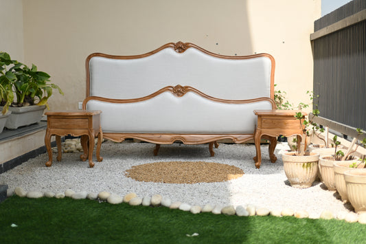 White sofa with wooden frame in an outdoor setting with plants and stones.