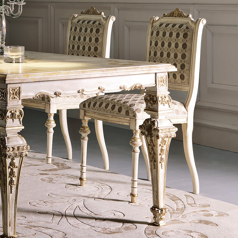Elegant dining table and chairs with intricate designs in a room with gray walls and a patterned rug.