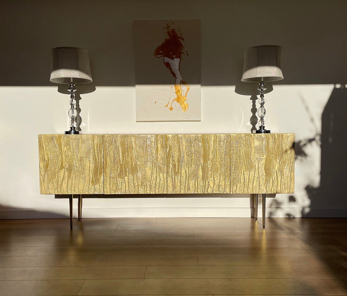 Gold sideboard with two lamps and a painting in a room setting