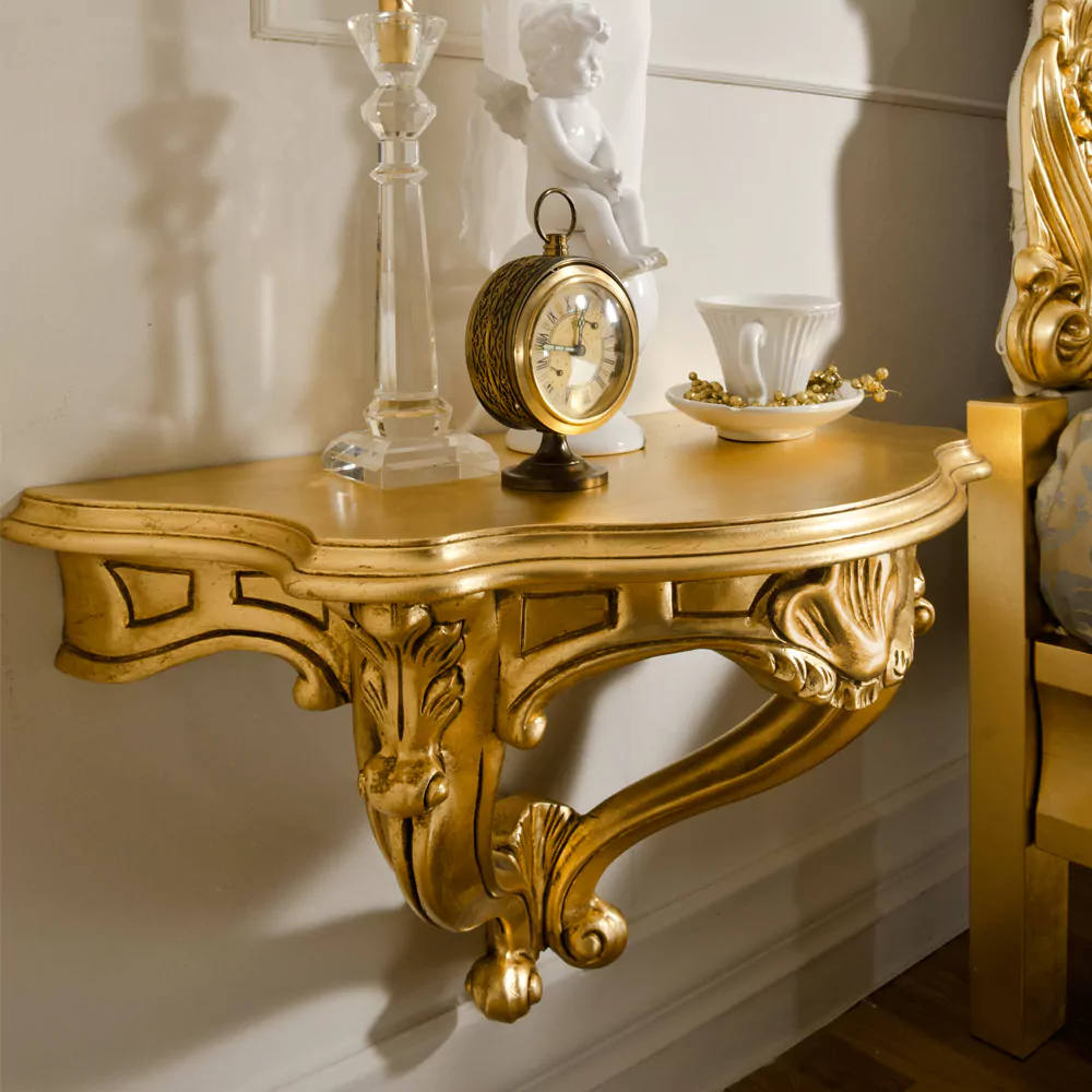 A gold leaf wall mounted console with intricate carvings, displayed in a room setting with decorative items on top.