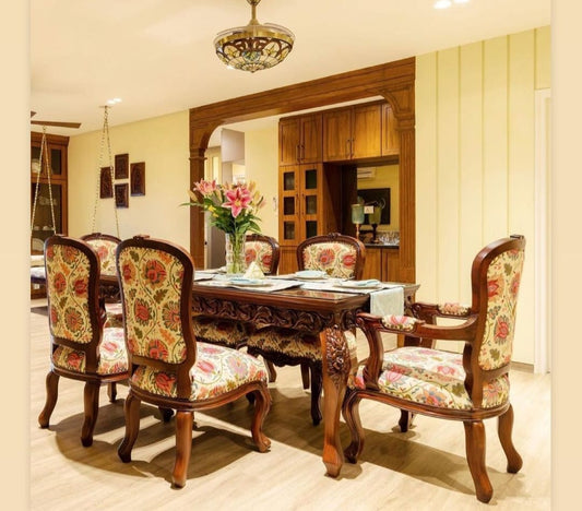 A Victorian-style 6-seater dining set with floral upholstered chairs and a wooden table, placed in a room with elegant decor.