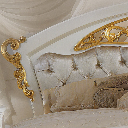 An ornate luxury bed featuring a tufted champagne-gold velvet headboard with elaborate gilded scrollwork side supports and a matching gold decorative arch on the wall, styled with cream and patterned pillows under draped white fabric.
