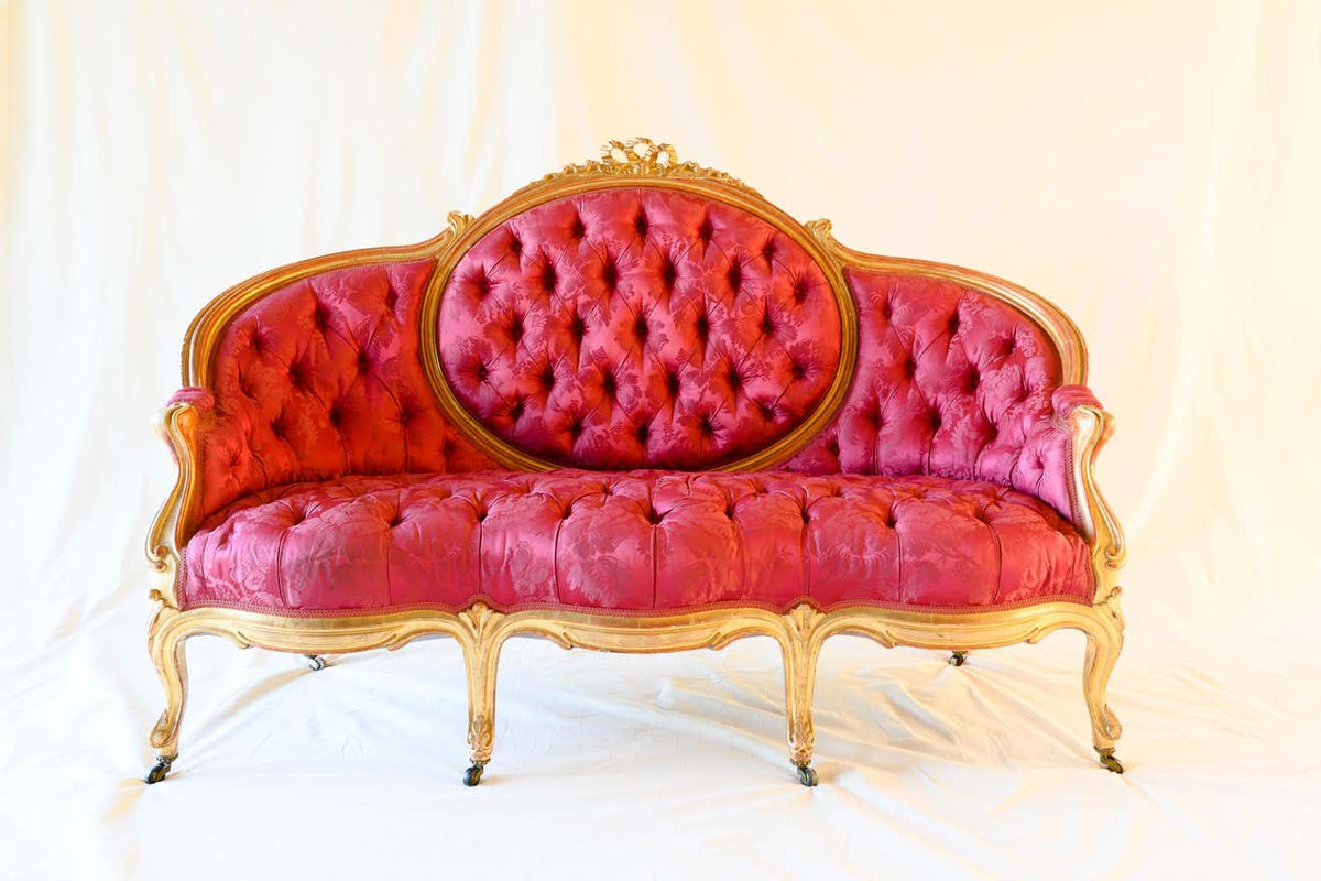 A three-seater crimson sofa with antique gold finish on the frame and tufted upholstery.