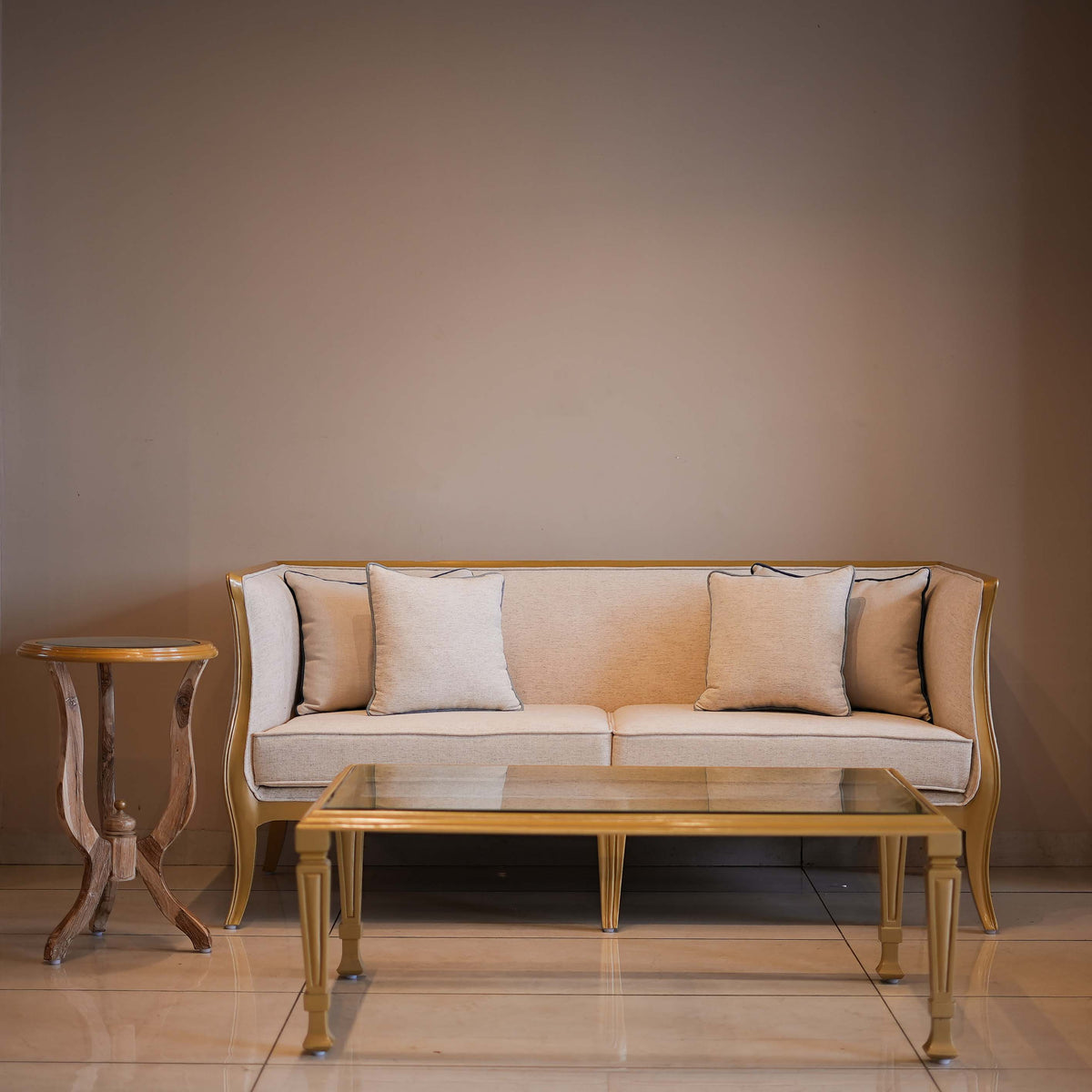 Beige sofa with cushions in a room with a plain wall and wooden side table.