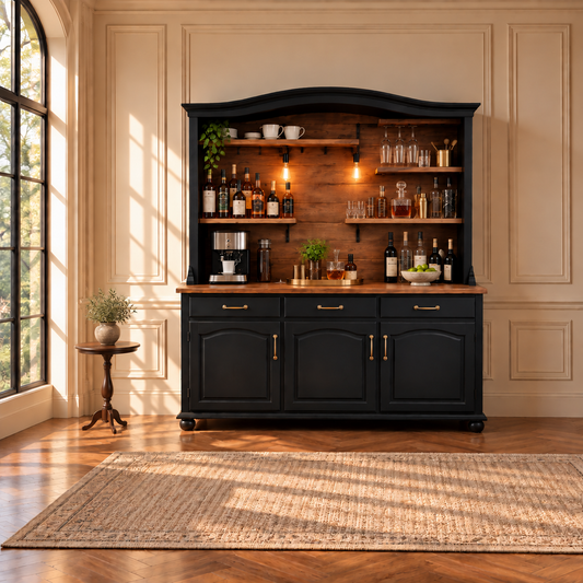 A tall black bar hutch with a warm wood finish and brass hardware, styled with bottles, glasses, and bar accessories, set in a sunlit room with a wood floor and a woven rug.