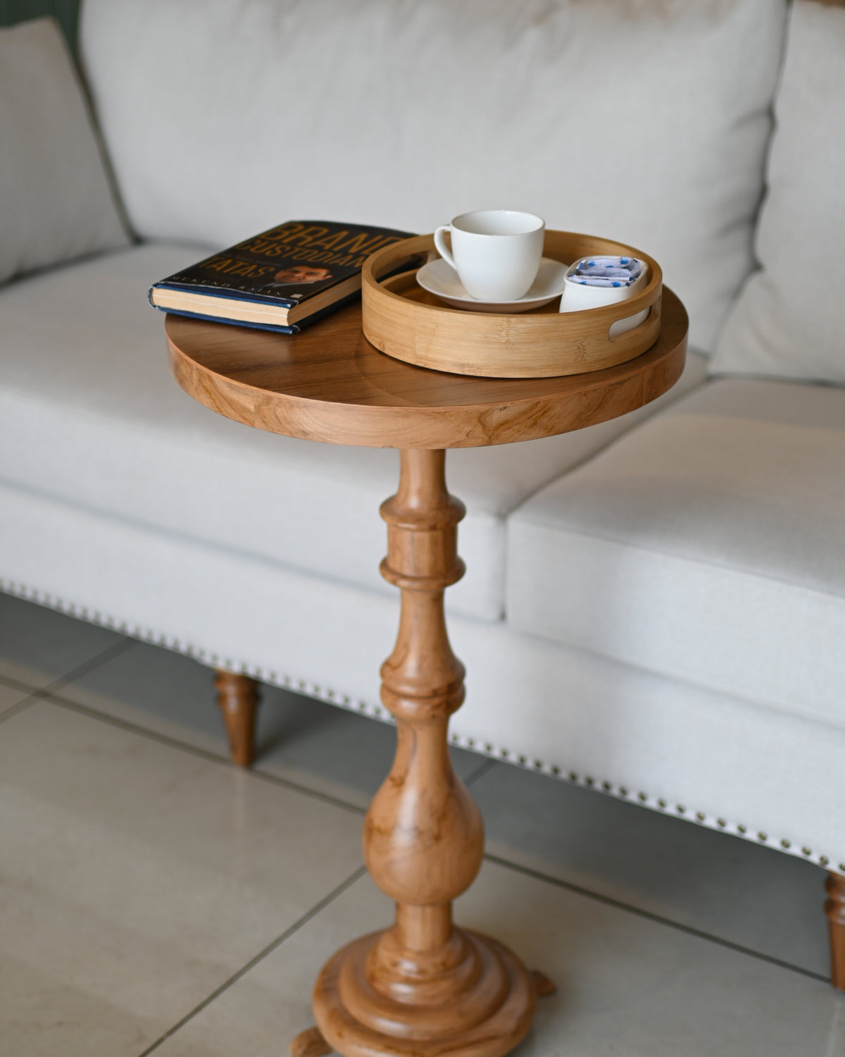 Wooden side table with a tray holding a cup, saucer, and book against a white sofa.