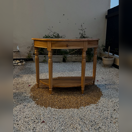 Wooden side table with a single drawer and open shelf on a gravel surface.