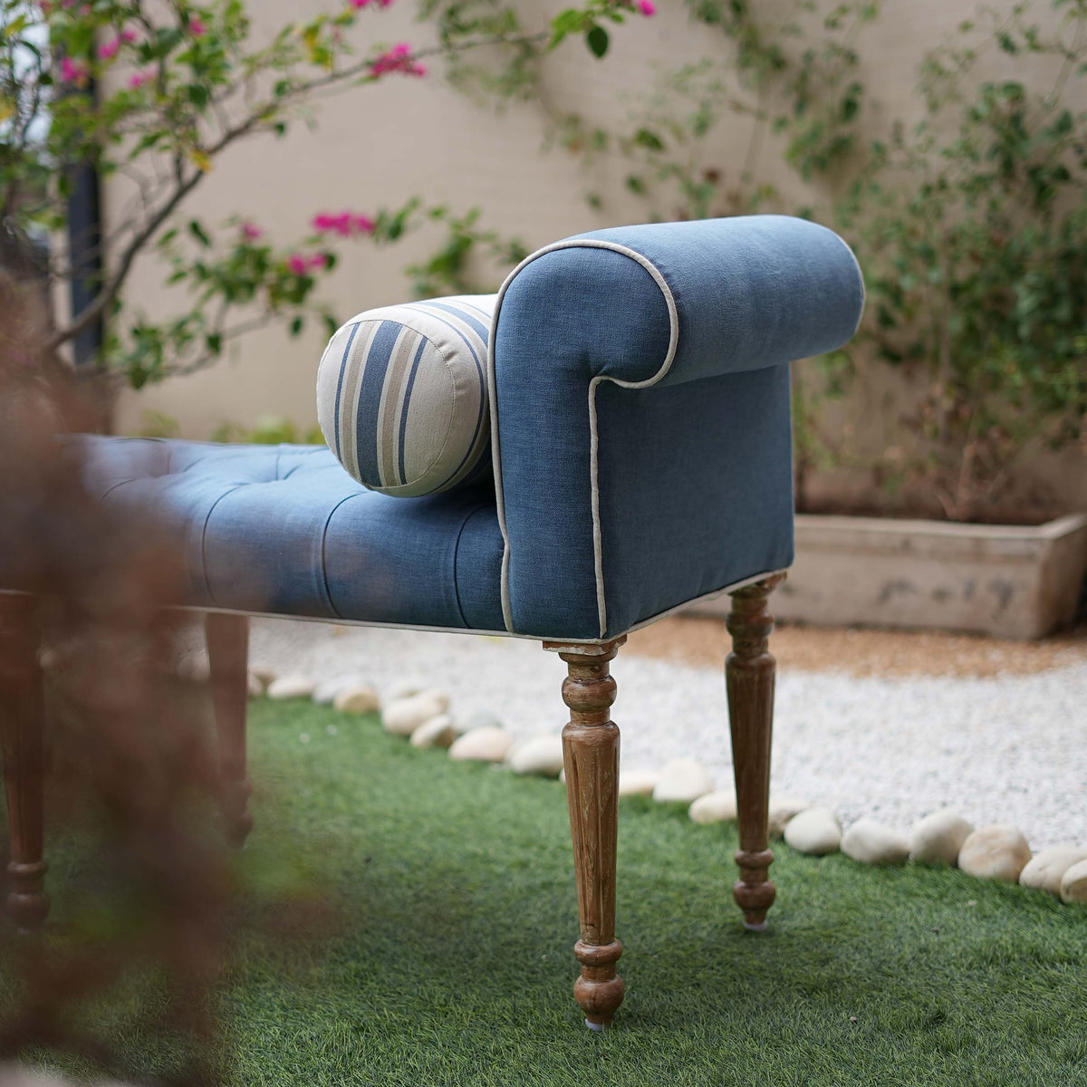 Blue tufted bench with wooden legs in an outdoor setting