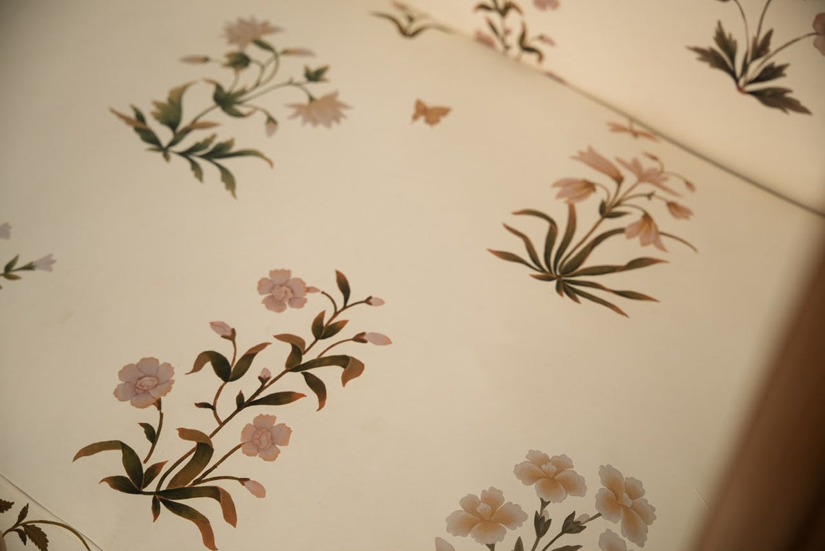 A close-up of a cream-colored wallpaper or fabric featuring a vintage floral pattern with pink blossoms and green-brown leaves.