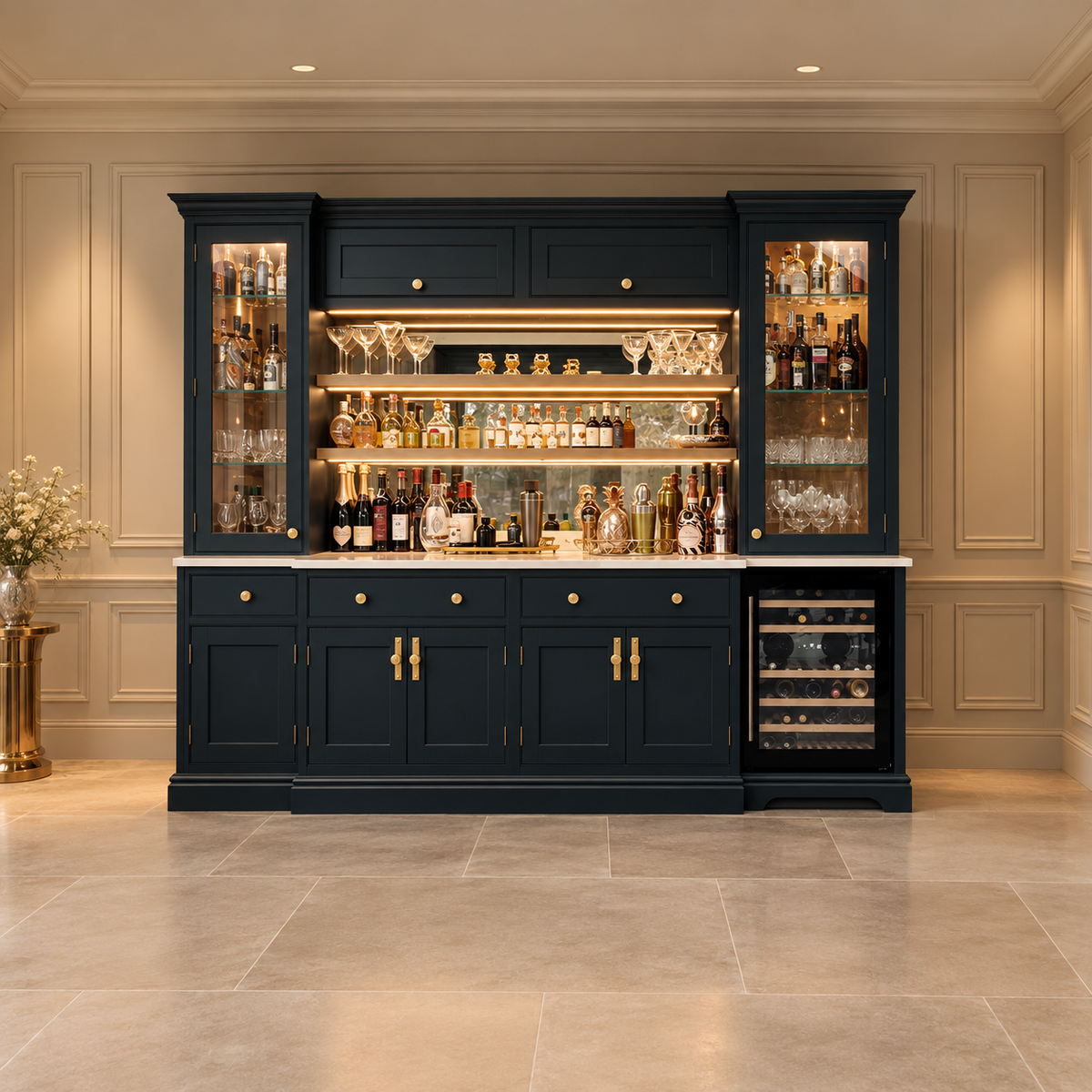A large navy blue built-in bar cabinet with glass-front side cabinets, illuminated shelves stocked with bottles and glasses, a marble countertop, and a built-in wine cooler on the right, shown in a luxury interior with beige paneled walls and stone tile flooring.