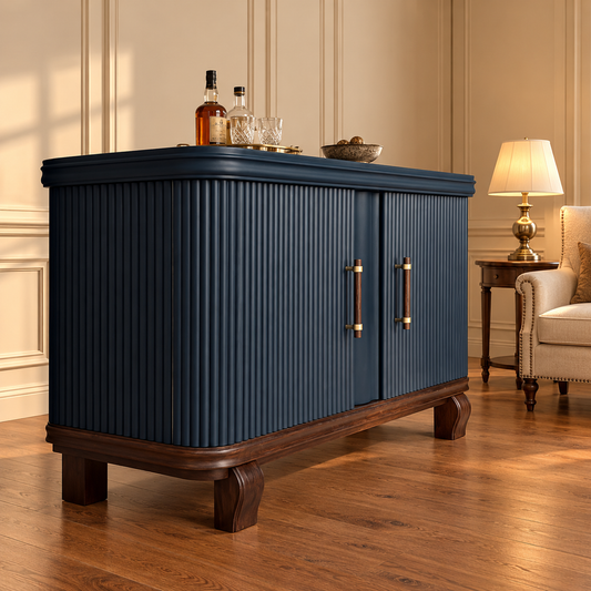 A dark navy blue ribbed cabinet with brass handles and a dark wood base, styled in a warm, elegant living room next to a lamp and armchair.