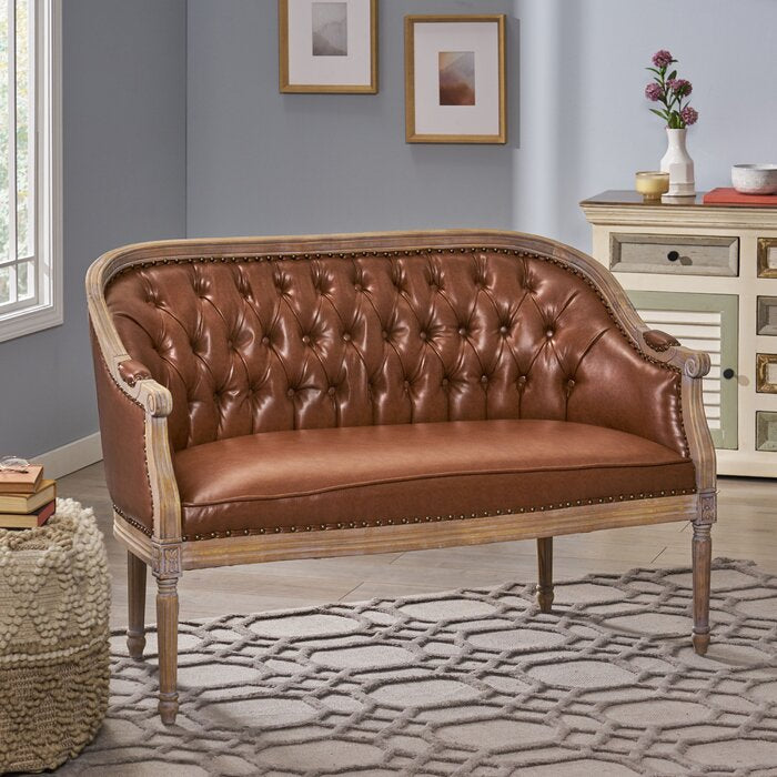 A brown leather bench sofa with tufted backrest and seat, placed in a room with a patterned rug and decorative wall art.