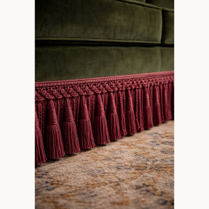 Green velvet sofa with a red tassel trim on a textured surface