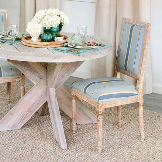 A rustic elegance chair with blue and white striped fabric on a wooden chair frame, placed next to a wooden table with a floral arrangement on top.