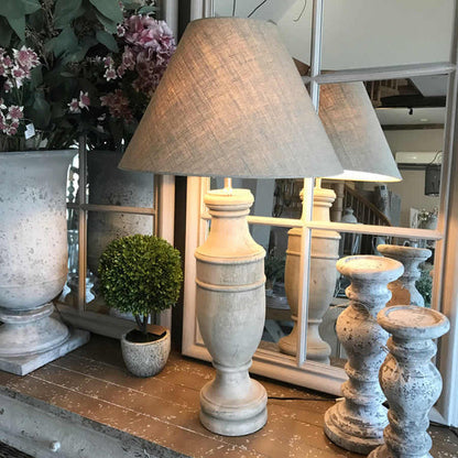 A beige Surahi Elegance French Finish Table Lamp with a traditional shape, displayed in a room setting with decorative items and a mirror in the background.