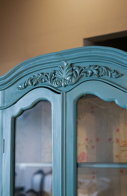 Teal armoire with decorative carvings on a blurred background