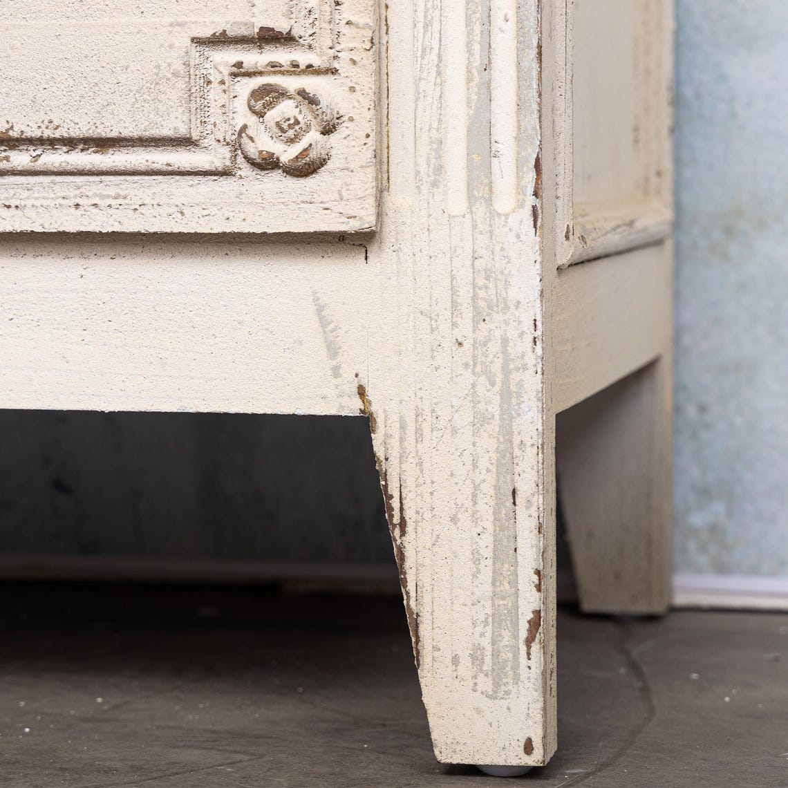Close-up of a distressed wooden cabinet corner with decorative carvings.