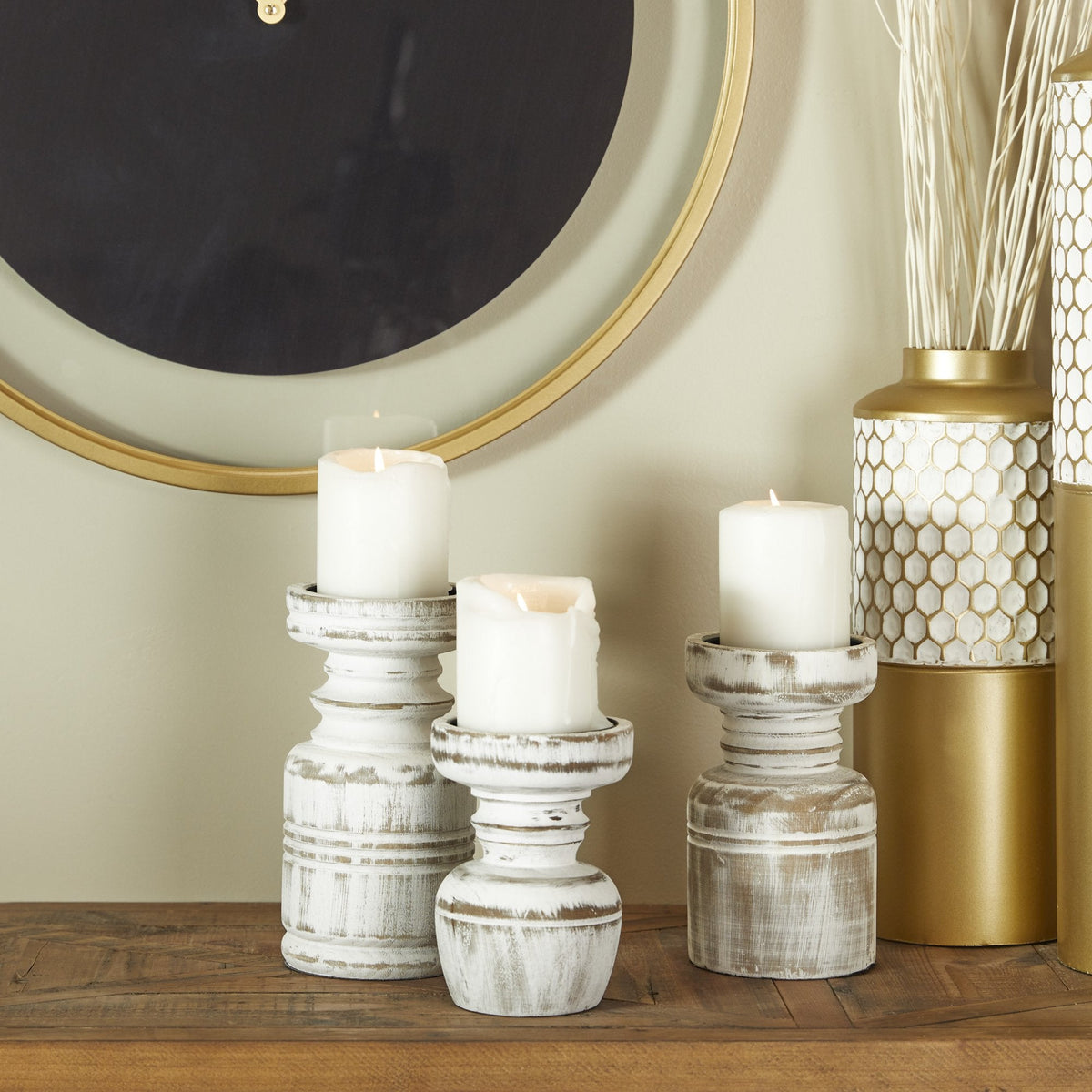 Three distressed white wooden candle holders in varying heights, with candles on top, placed on a table alongside decorative items.
