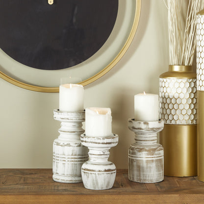 Three distressed white wooden candle holders in varying heights, with candles on top, placed on a table alongside decorative items.