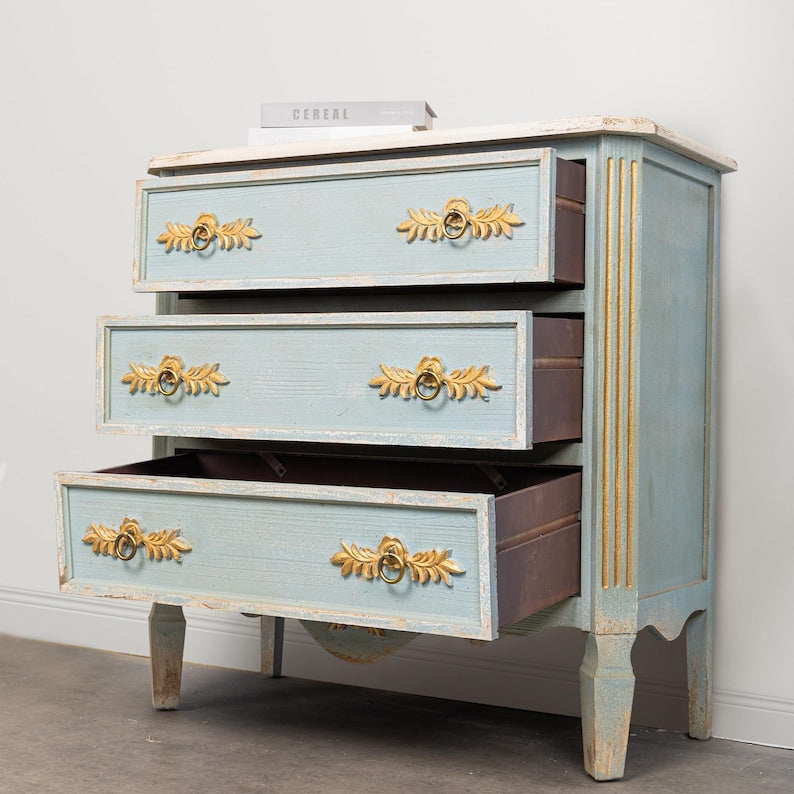 A blue wooden buffet cabinet with three drawers, featuring gold floral carvings on the handles and edges.