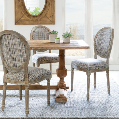 A set of three dining chairs with a geometric patterned fabric upholstery on a wooden dining table, placed in a bright room setting.