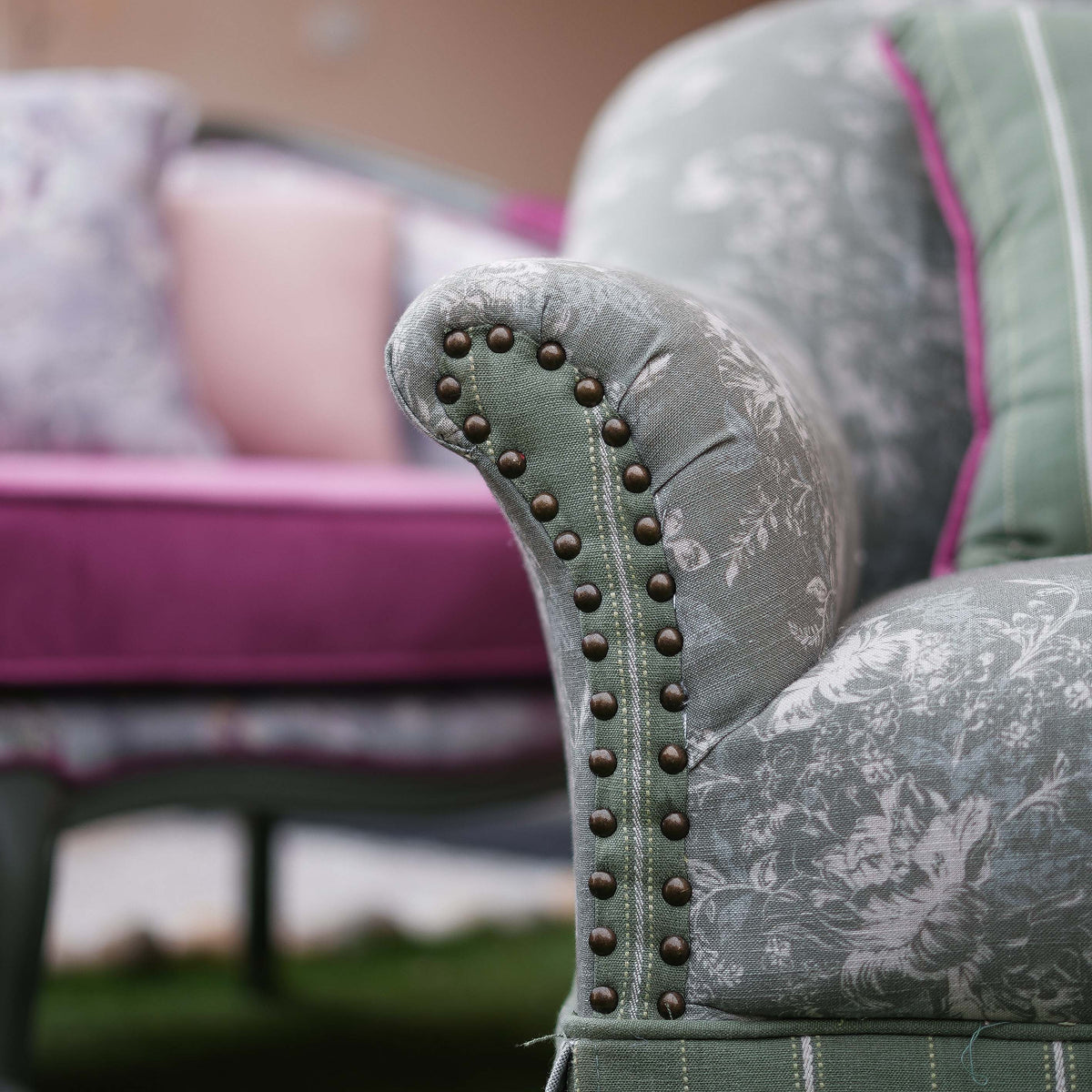 Close-up of a floral-patterned chair with studded armrests, blurred background