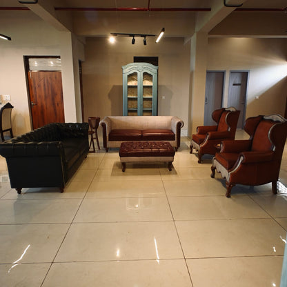 Lounge area with vintage furniture including a black sofa, brown armchairs, and a wooden cabinet.