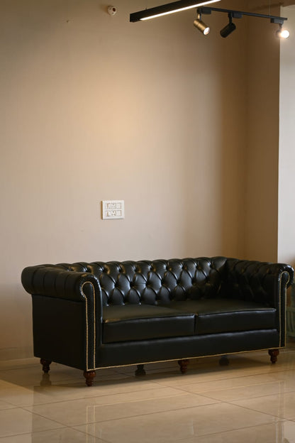 Black leather sofa in a room with beige walls and tiled floor.