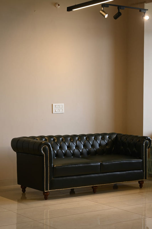 Black leather sofa in a room with beige walls and tiled floor.