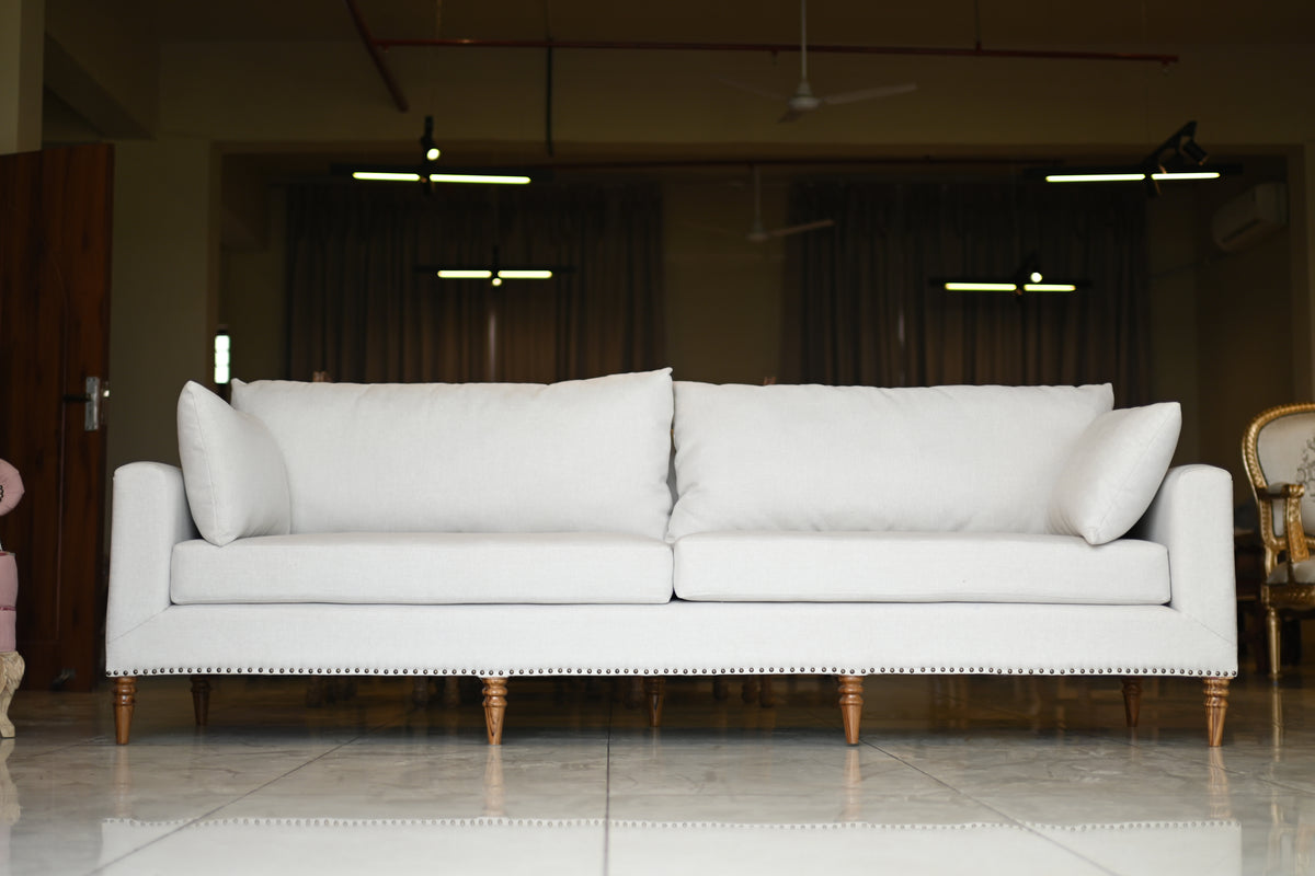 White sofa with wooden legs in a room with dark curtains and ceiling lights.