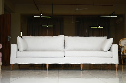 White sofa with wooden legs in a room with dark curtains and ceiling lights.