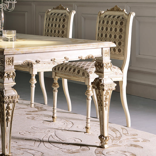 Elegant dining table and chairs with intricate designs in a room with gray walls and a patterned rug.