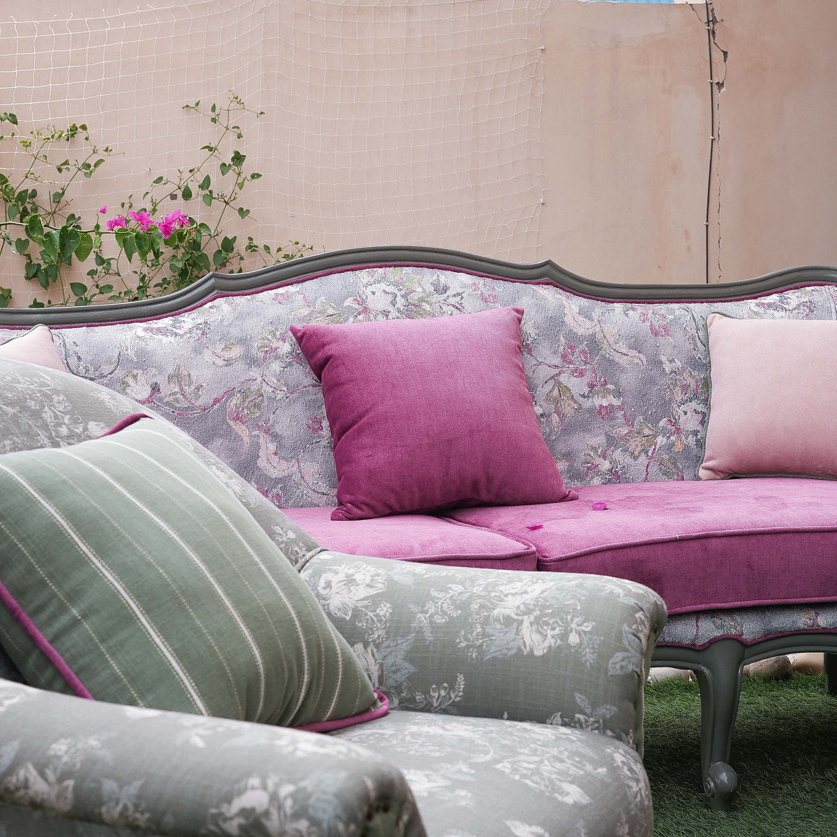 Floral-patterned sofa with pink and green cushions against a neutral wall.