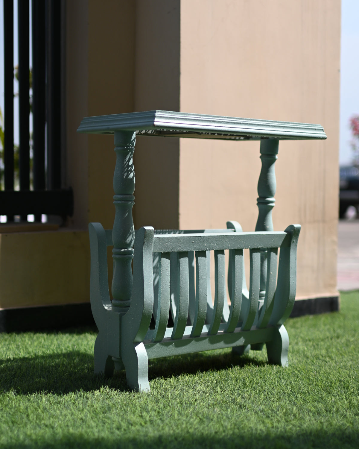 Green metal magazine rack with a small table on grass