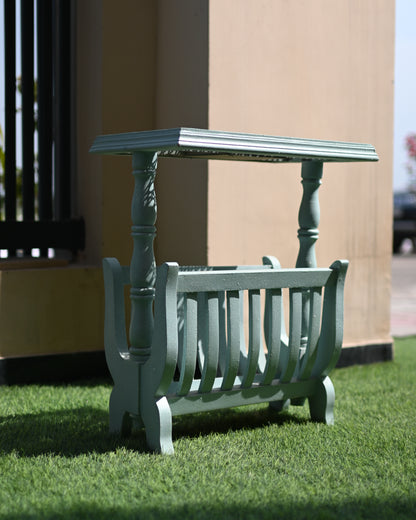 Green metal magazine rack with a small table on grass