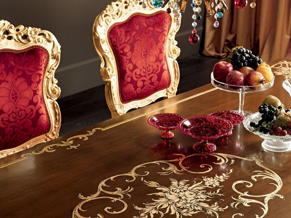 Decorative table setting with red chairs, fruit, and jewelry on a wooden table.