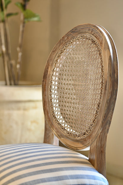 Wooden chair with wicker backrest and striped cushion in a room setting.