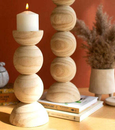 Wooden candle holder on a table with a candle and books in the background.