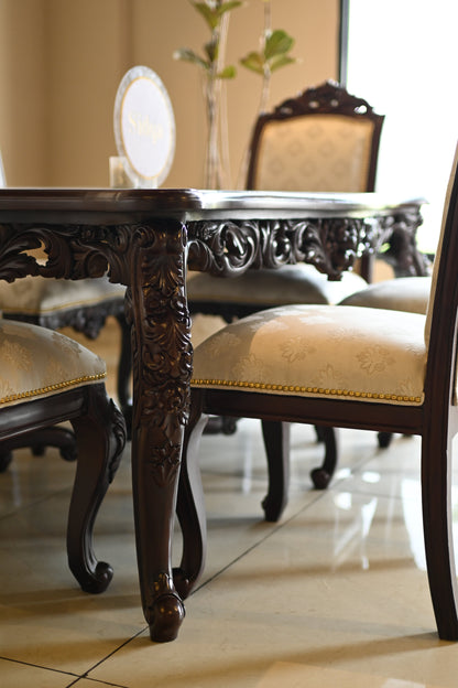 A luxurious dining ensemble with a hand-carved wooden dining table and six upholstered chairs with golden studding and floral crests.