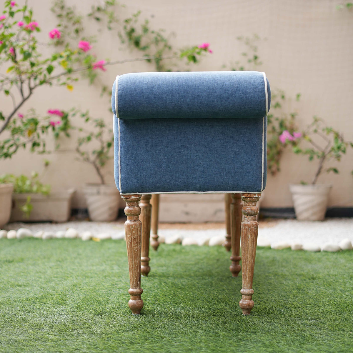 Blue upholstered stool with wooden legs on a grassy area with plants in the background