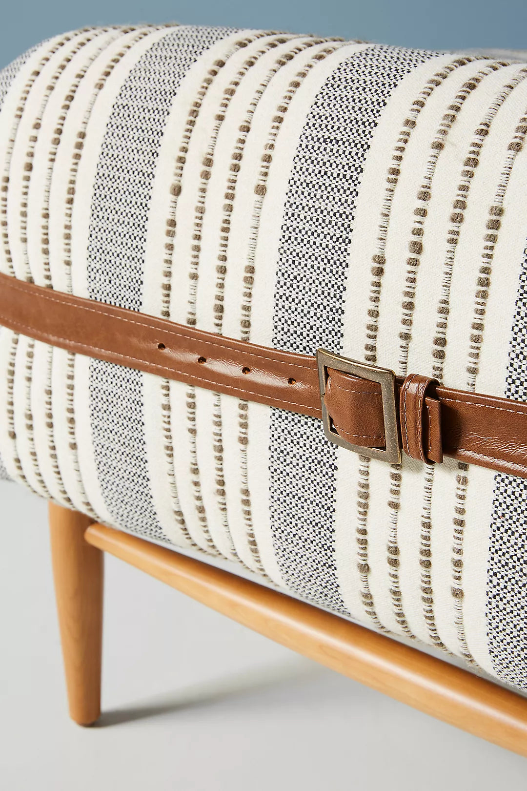 Striped fabric bench with a brown leather strap on a light gray background