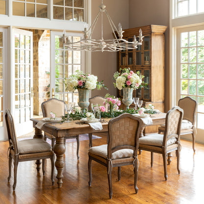 A set of elegant dining chairs with beige fabric upholstery and ivory cushions, around a wooden dining table, in a room with a chandelier and large windows.