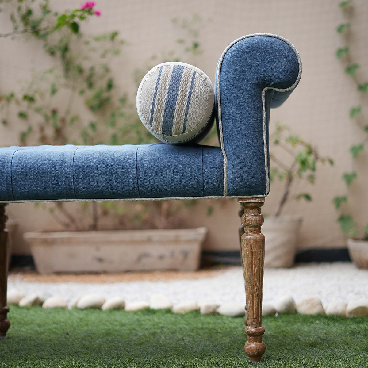 Blue upholstered bench with striped cushion on a grassy area with plants in the background