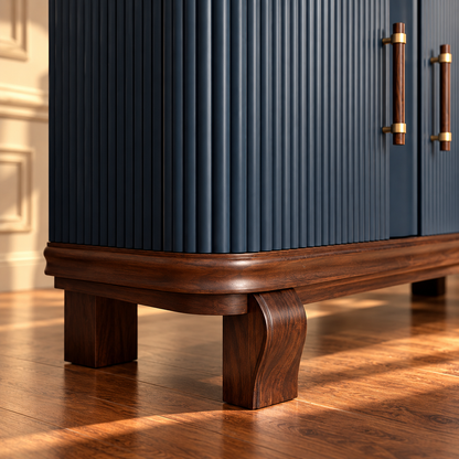 A close-up of a modern cabinet with dark blue vertically fluted doors, a rich dark brown wooden base and legs, and brass handles, set on a warm hardwood floor with sunlight casting shadows.