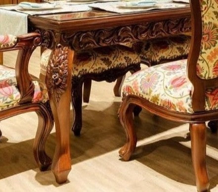Dining table with ornate carvings and floral-patterned chairs in a room.