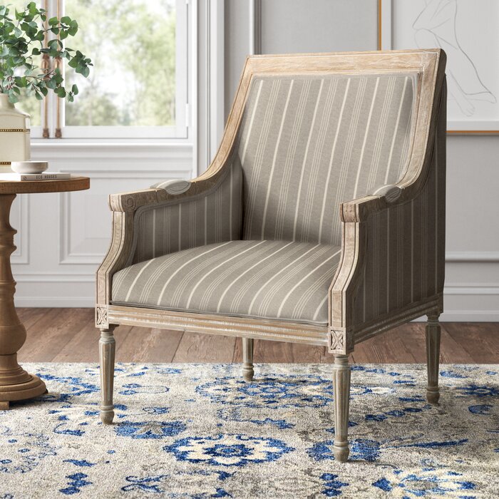 A beige Sidqa vintage charm armchair with a striped pattern on linen fabric, featuring a natural distressed finish and wooden legs, placed on a blue and white patterned rug.