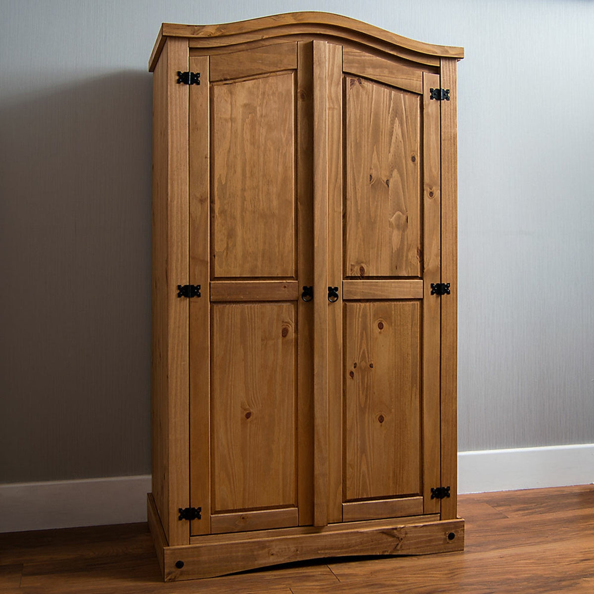 A wooden armoire with two doors, metal hinges, and a curved top, placed against a indoor background.