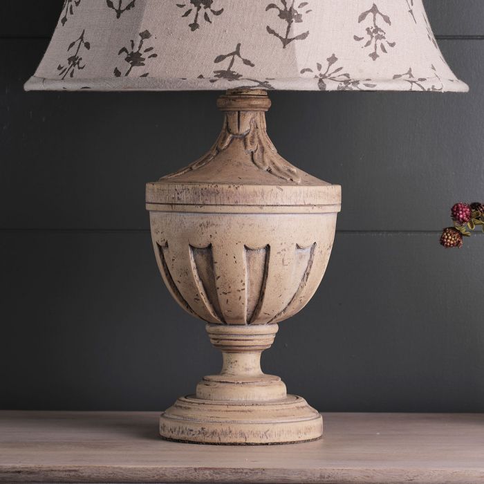 A beige table lamp with a floral patterned shade, featuring a fluted curve base reminiscent of a classical Urn design.