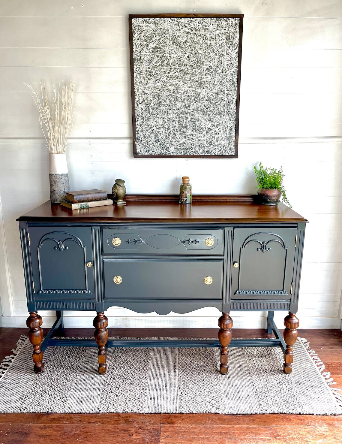 A Teal blue buffet cabinet with carved details and brass knobs, displayed in a room setting with decorative items on top.