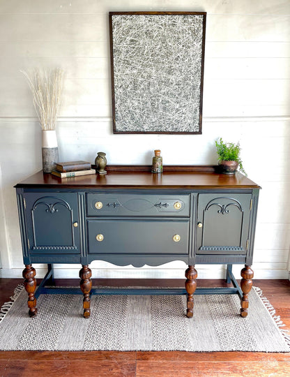 A Teal blue buffet cabinet with carved details and brass knobs, displayed in a room setting with decorative items on top.